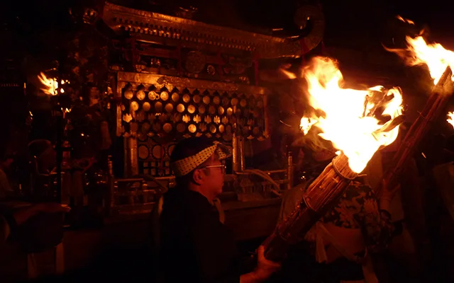 A man holding a fire-torch walks by the portable shrine (mikoshi) of the festival.
