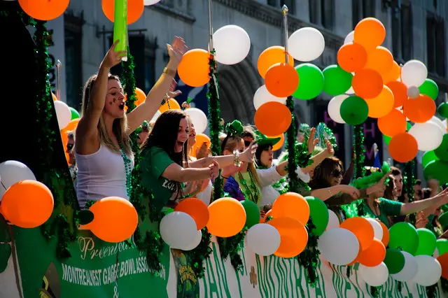 Partying crowd, holding balloons at the colors of the Irish flag (green, white, orange), on a parade chariot.