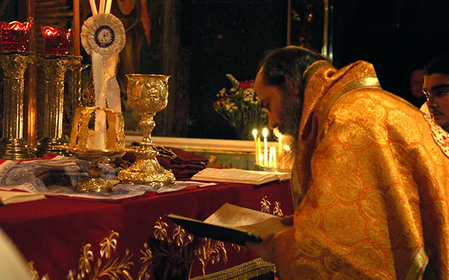 Orthodox priest reading prayers in front of the crucifixion altar.