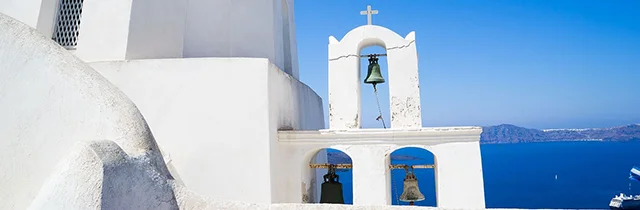 White belfry of a Greek Orthodox church with the gorgeous background of Santorini island landscape.
