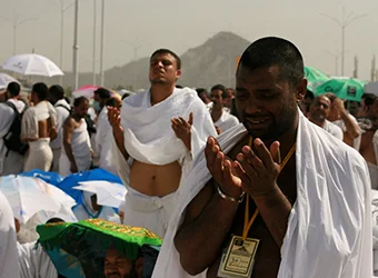 Pilgrims in white garments (ihram) are praying.