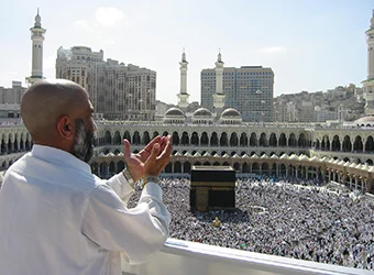 A man praying with extended hands to the Kaaba.