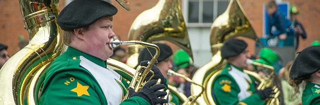 Members of an Irish marching band in green uniforms participating in a St. Patrick's Day parade.