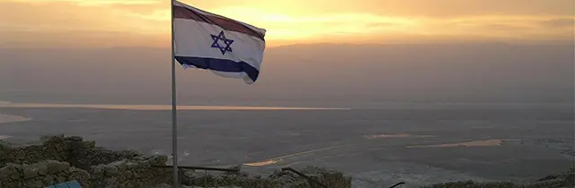The flag of Israel at a background of an evening wide landscape.