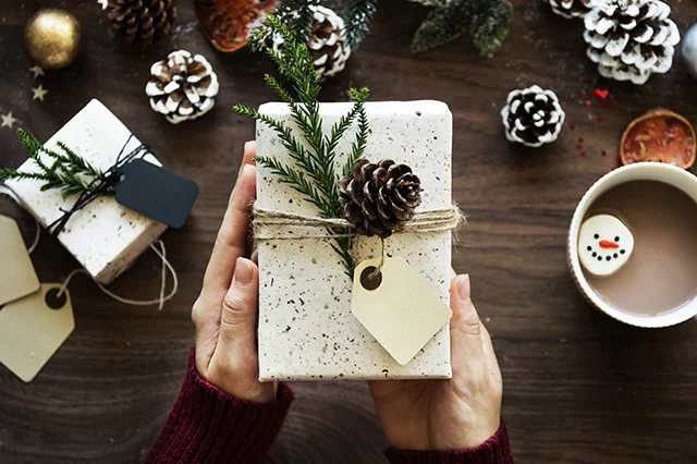 Hands holding a Christmas gift in front of other festive decorations.