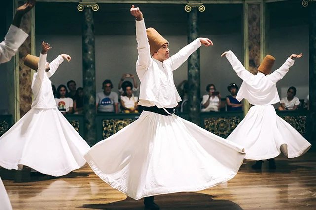 Three dervishes are conducting the Sufi (wringling) dance with their audience at the background.