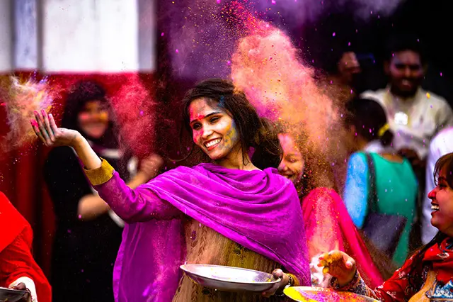 A female participant of Holi Festival smeared with colors, throws dried powdered colors contained in a platter.