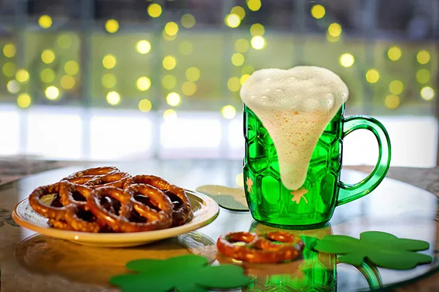 A plate with Irish pretzels and a pint of green Irish beer on a table decorated with shamrocks.