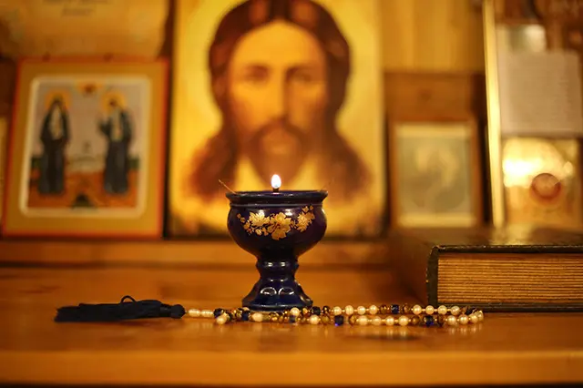 A lit lamp, a prayer bead, and a Bible in front of a series of Christian Orthodox icons.