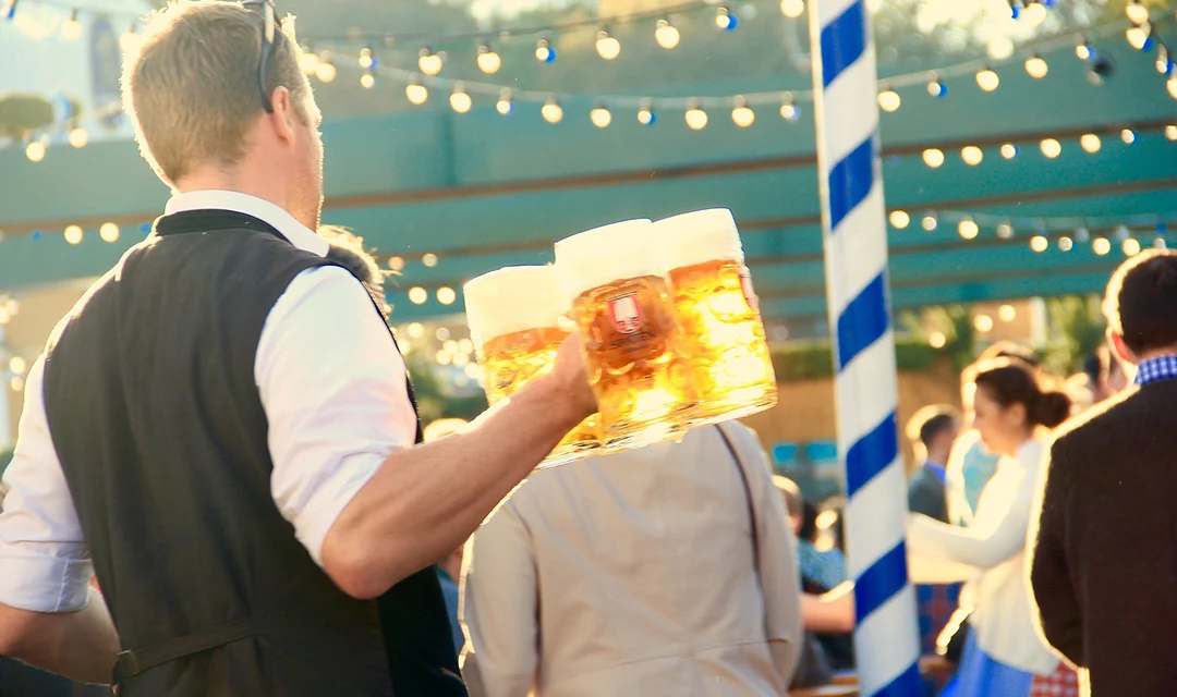 A waiter is serving large glasses of beer in a crowded open-air pub during Octoberfest.